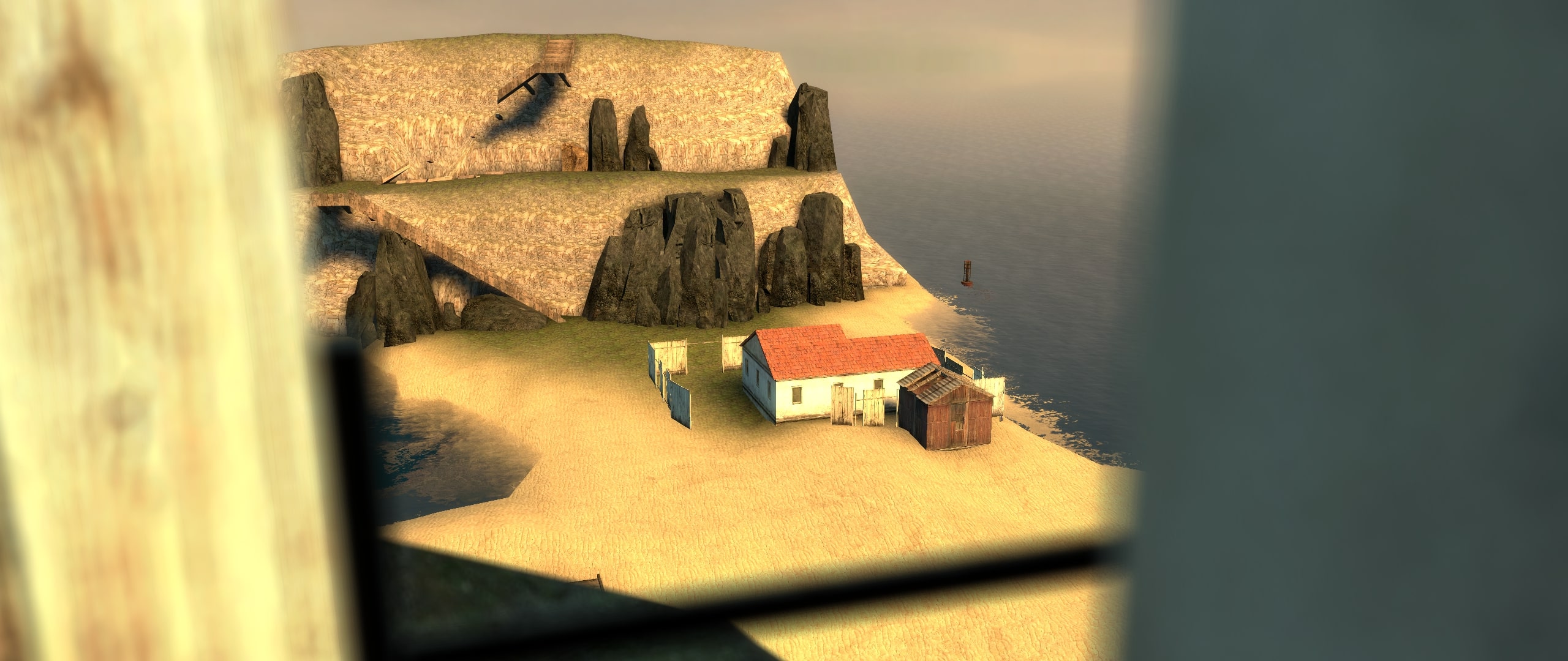 A view from a window looking down at a house and shed in a beach valley, and a wooden staircase up to a cliff face.